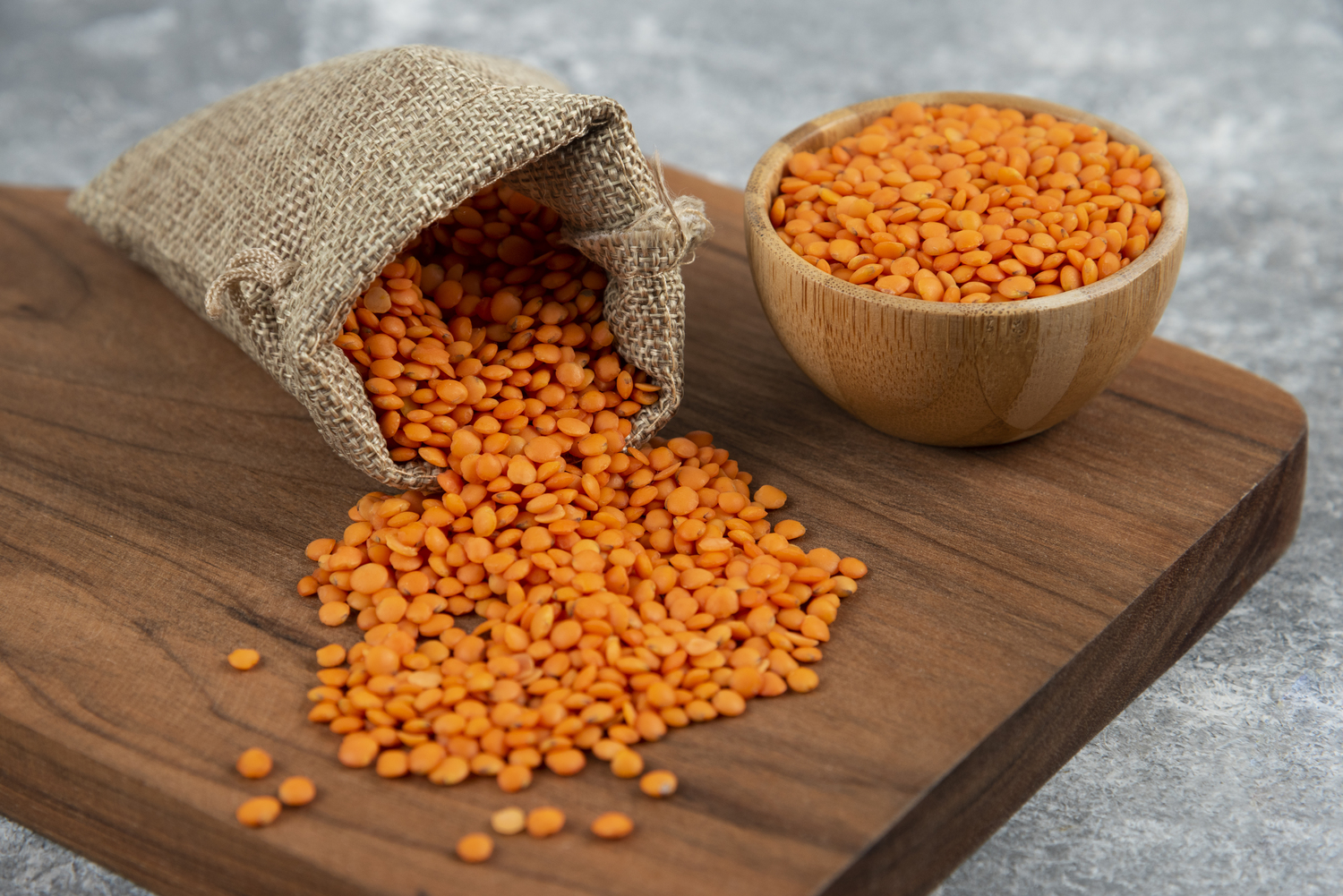 Bowl and sackcloth of red raw lentils on wooden board